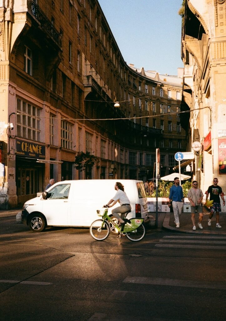 Cyclist crosses street in front of buildings and van.
